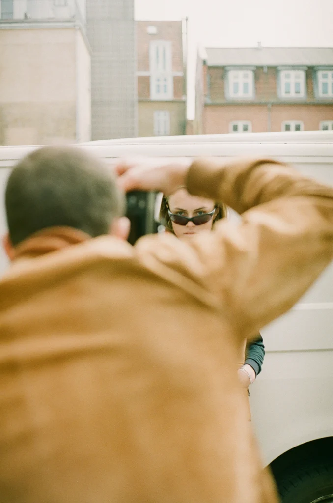 Photographer capturing a model wearing sunglasses, with a cityscape in the background.