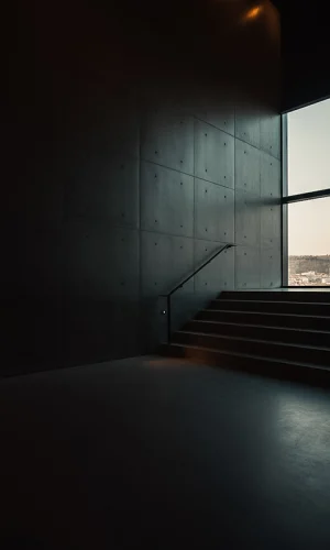 Mørkt minimalistisk interiør med trappe og stor rude med udsigt over landskab